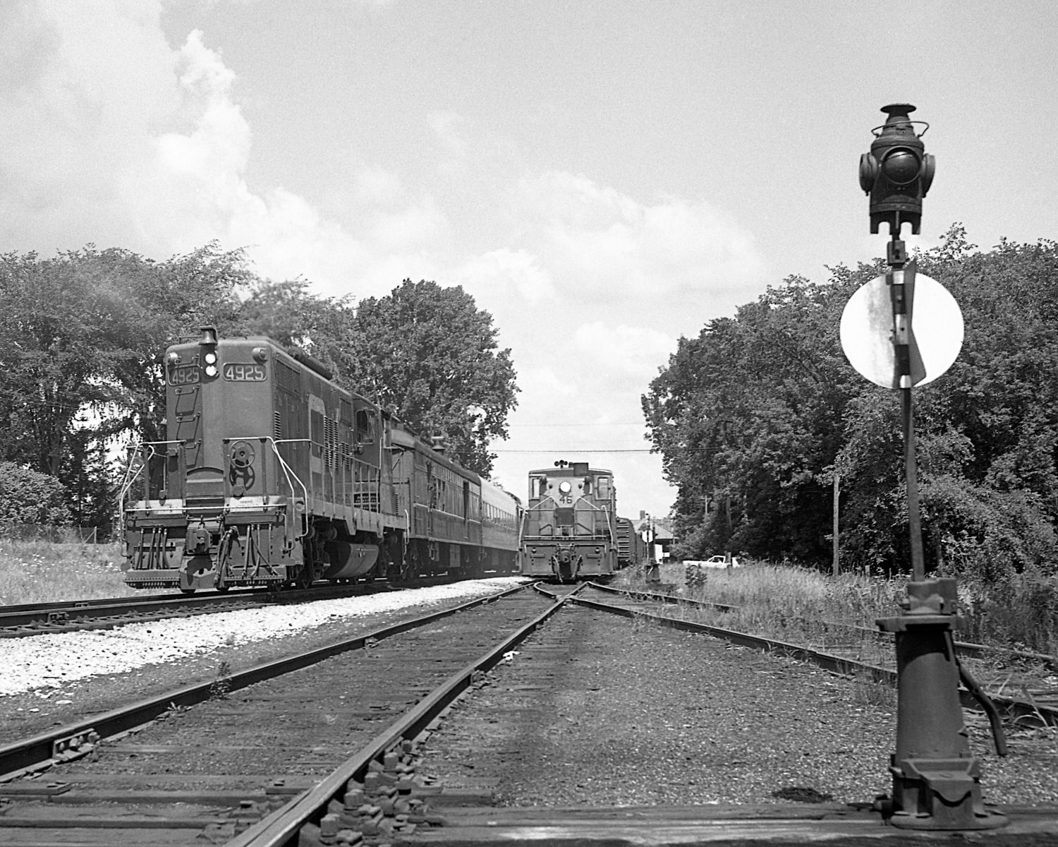 St. Johnsbury & Lamoille County Railroad 70 tonners #46, 54 & Montpelier & Barre #19 switching  at StJ&LC's yard in Swanton, VT while a Central Vermont passenger train goes by. Mid to late 1960's. (8x10)