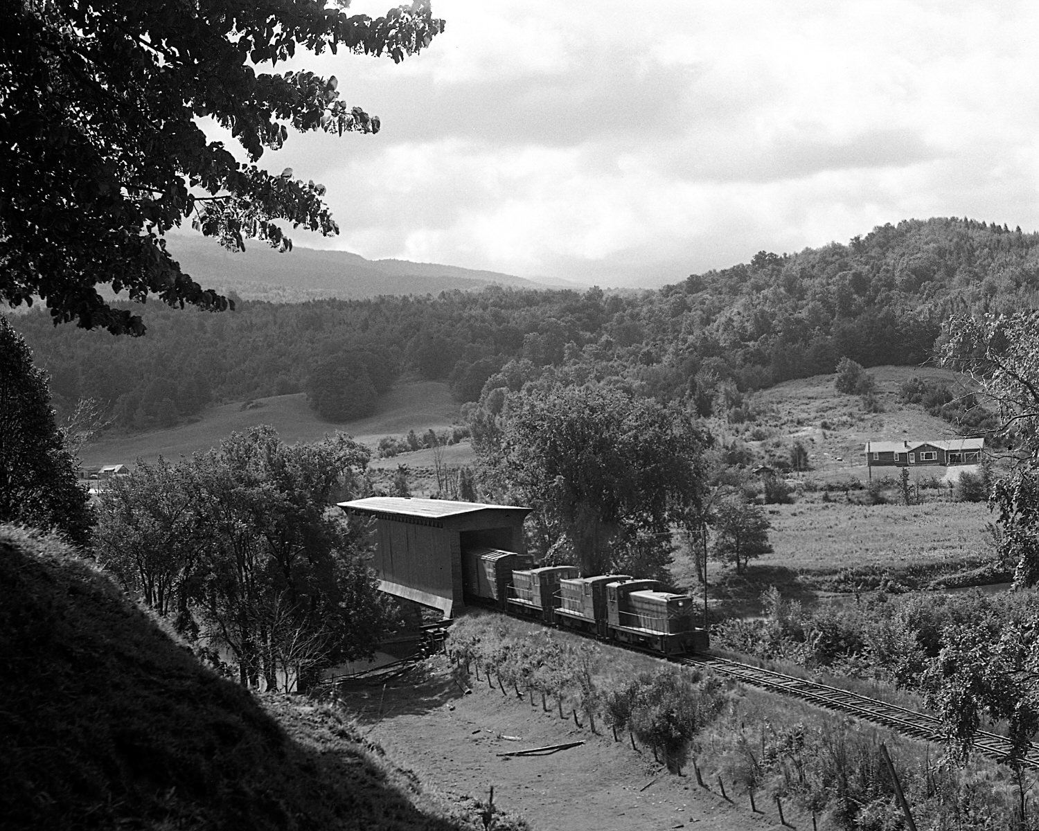 St. Johnsbury & Lamoille County Railroad train with 70 tonners Montpelier & Barre #19, StJ&LC #54 and #46 pass through the covered bridge at Cambridge Juncion, Vermont. Mid to late 1960's. (8x10)